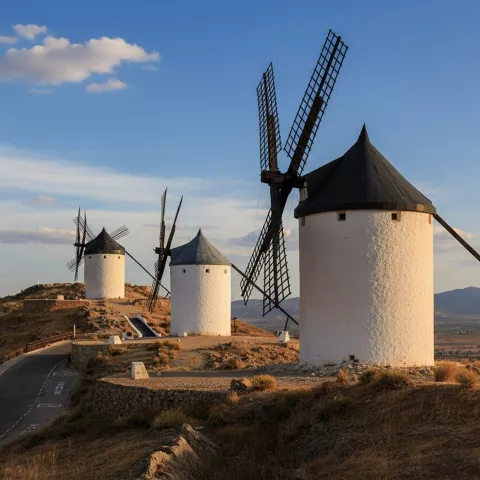 Molinos blancos sobre colina al atardecer con carretera sinuosa.