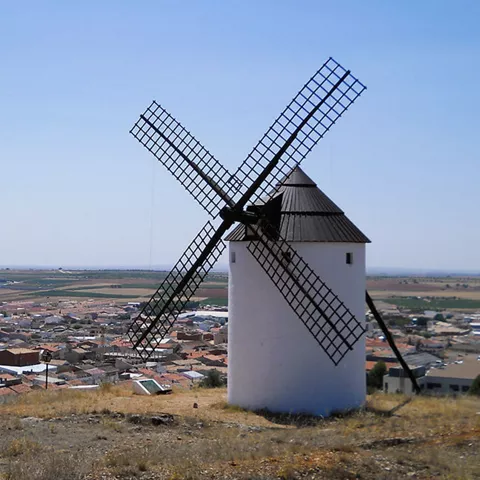 Molino de viento en primer plano con un pueblo extendido al fondo.