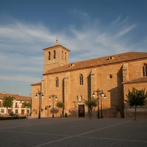 Gran iglesia de piedra en una plaza amplia, iluminada por luz cálida al atardecer.