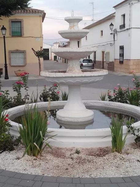 Fuente de piedra blanca en la plaza de Montalvos rodeada de flores y viviendas tradicionales.