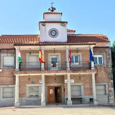 Edificio municipal con reloj central, balcón corrido y cuatro banderas