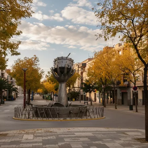 Rotonda con escultura de una mano sosteniendo un tambor, en avenida arbolada con hojas otoñales.