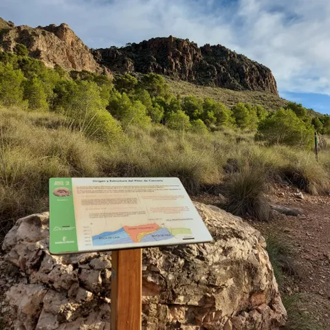 Panel informativo sobre formaciones geológicas frente a un relieve rocoso y vegetación mediterránea.