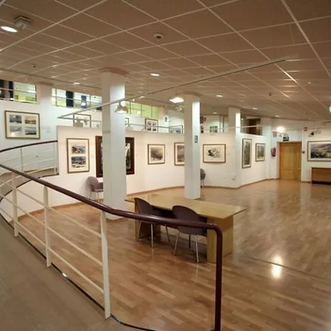 Sala de exposiciones con rampa curva, mesas y obras enmarcadas.