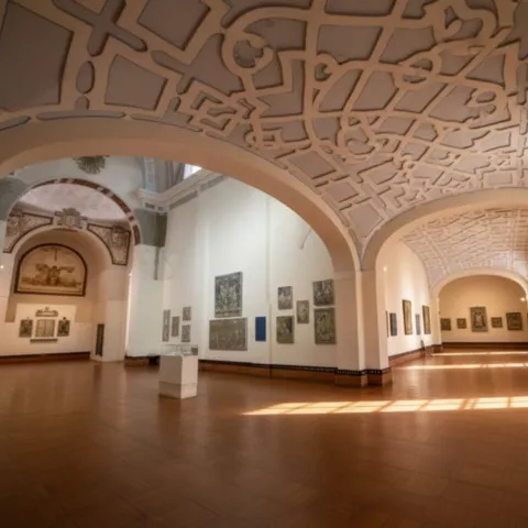 Sala con bóveda decorada y paneles de azulejos, con luz entrando por las ventanas.