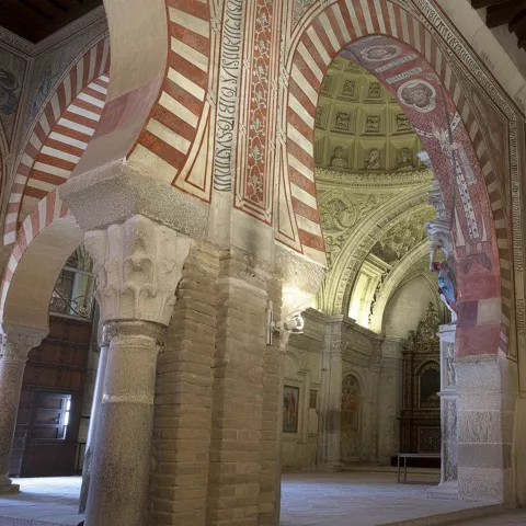 Interior con arcos de herradura y pinturas murales en tonos rojizos.