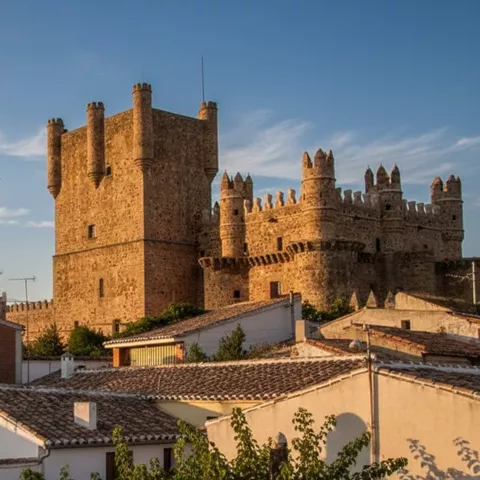 Castillo medieval iluminado al atardecer sobre tejados de pueblo.