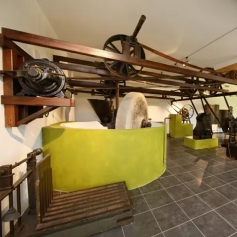 Maquinaria industrial antigua para molienda con piedra circular y engranajes metálicos.