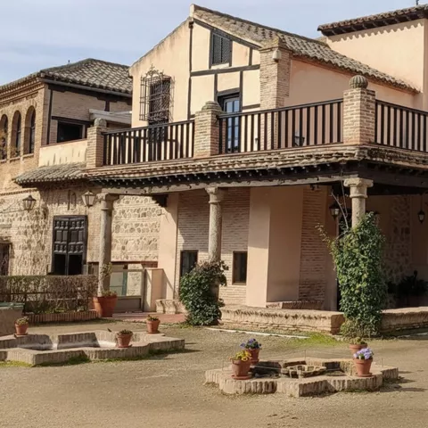 Patio de edificio histórico con columnas, balcón de madera y macetas.