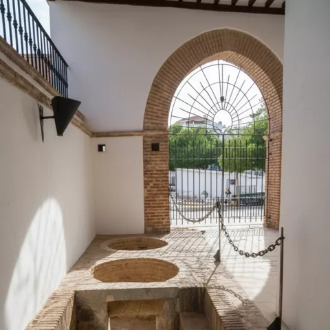 Pasillo con arcos de ladrillo, reja al fondo y restos de estructuras en el suelo.