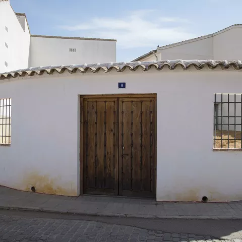 Fachada encalada con puerta de madera y ventanas con rejas.