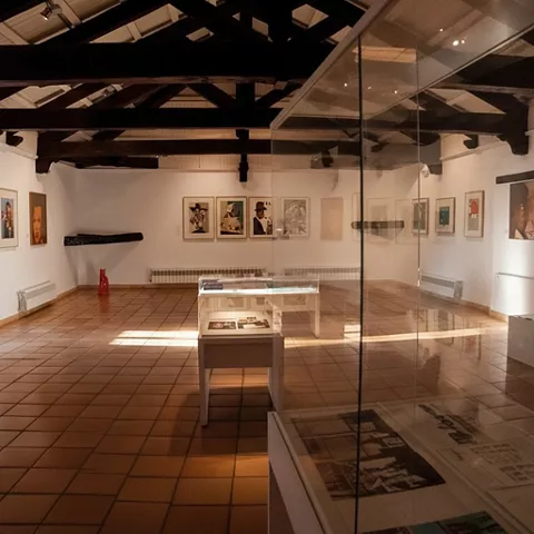 Sala con vigas vistas, obras en paredes y vitrina central.