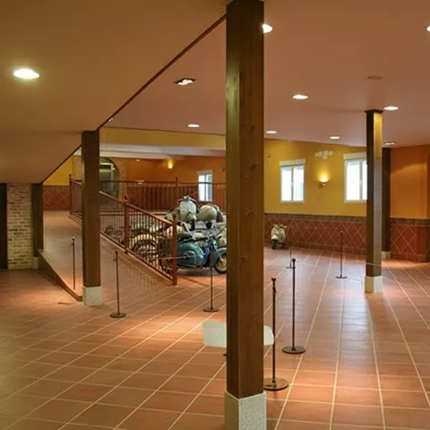 Sala amplia de museo con suelo de barro, columnas y motocicletas al fondo.