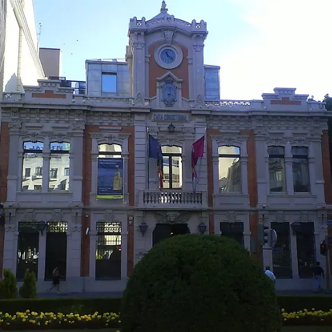 Fachada monumental de un edificio cultural con reloj central y banderas en el balcón.