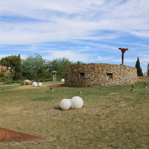 Espacio ajardinado con construcción circular de piedra y escultura metálica
