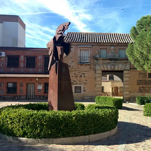 Escultura abstracta de metal frente a edificio histórico y jardines recortados