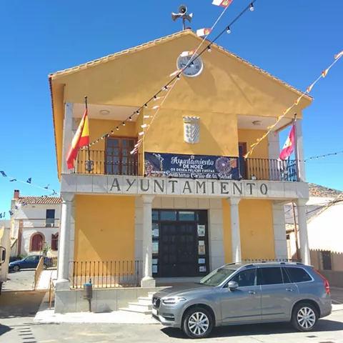 Fachada de ayuntamiento amarillo con reloj y coche aparcado