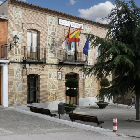 Fachada de casa consistorial con banderas y plaza con bancos