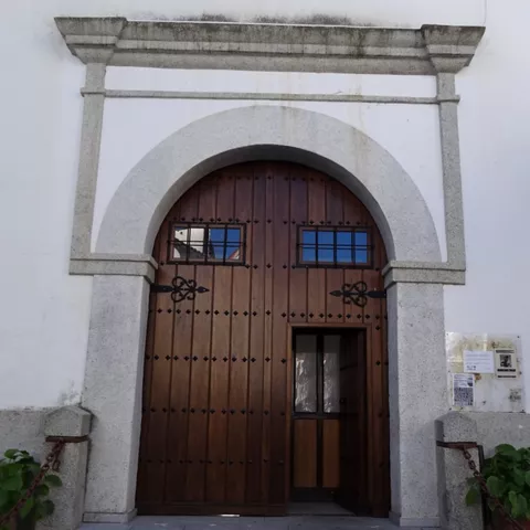 Puerta de madera con arco de piedra en fachada blanca.