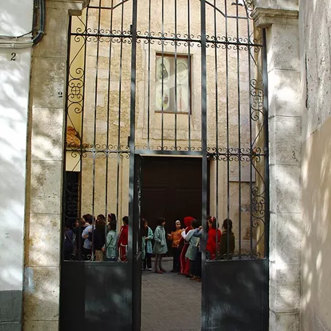 Puerta de hierro forjado abierta que da acceso a un patio interior con personas reunidas.