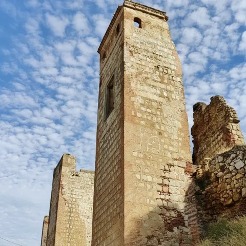 Torre de piedra en ruinas junto a restos de muralla