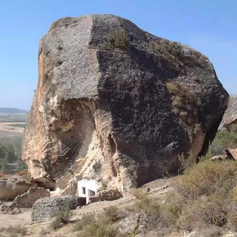 Gran bloque rocoso aislado con pequeñas construcciones en su base.
