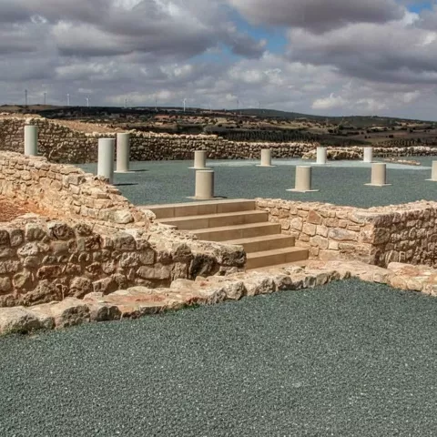 Recinto de ruinas con postes de piedra y nubes dramáticas.