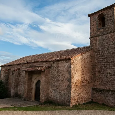 Iglesia rural de piedra con campanario cuadrado y tejado de teja bajo cielo azul.