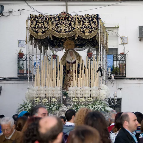 Paso procesional con imagen religiosa rodeado de cirios y multitud