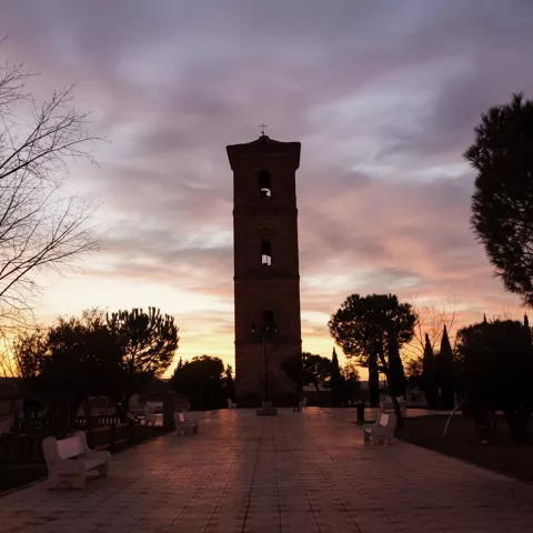 Silueta de torre sobre plaza con bancos al atardecer.