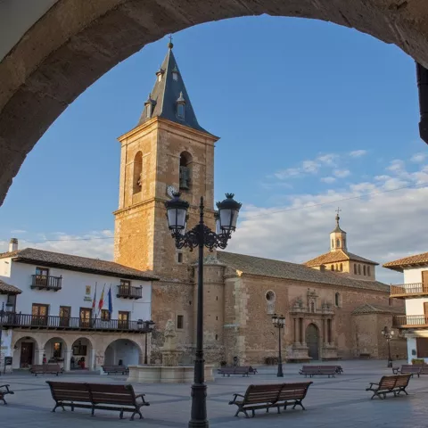 Soportales y casas con balcones de madera alrededor de una plaza con bancos.