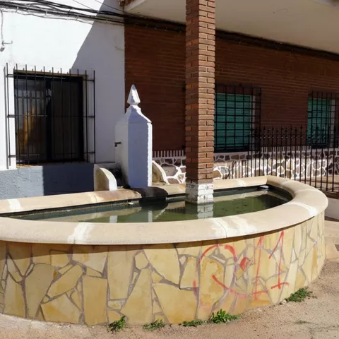 Fuente pública en Povedilla junto a edificio de ladrillo y viviendas tradicionales.