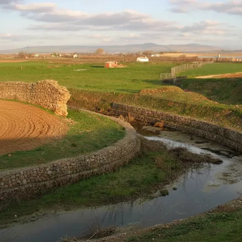 Río estrecho rodeado de praderas y bancales agrícolas al atardecer.