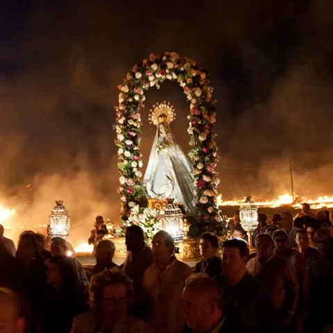 Imagen adornada con flores rodeada de fuego y asistentes.