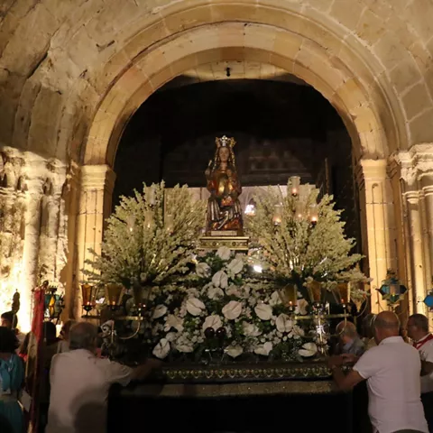 Paso procesional bajo arco de piedra con asistentes.