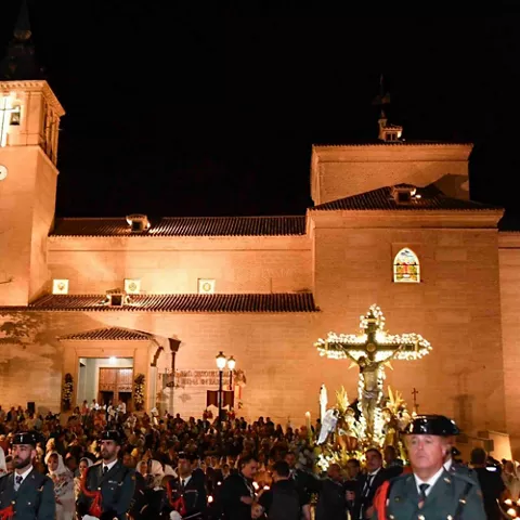 Procesión nocturna frente a un templo iluminado con una imagen religiosa al fondo.