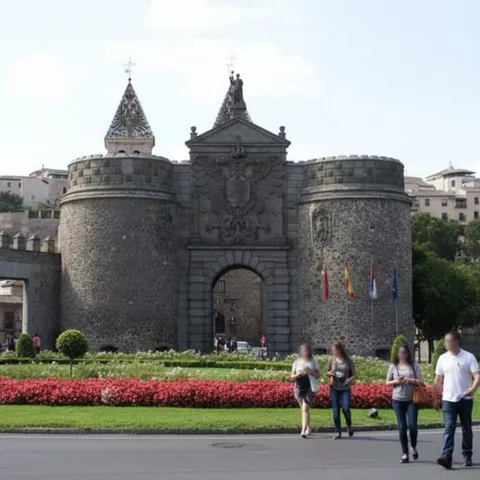 Entrada histórica rodeada de parterres florales y peatones cruzando.