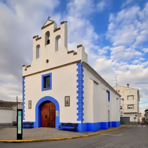 Vista de una iglesia de estilo barroco, con fachada blanca con detalles azules y una torre del reloj con cúpula, ubicada en una calle adoquinada.