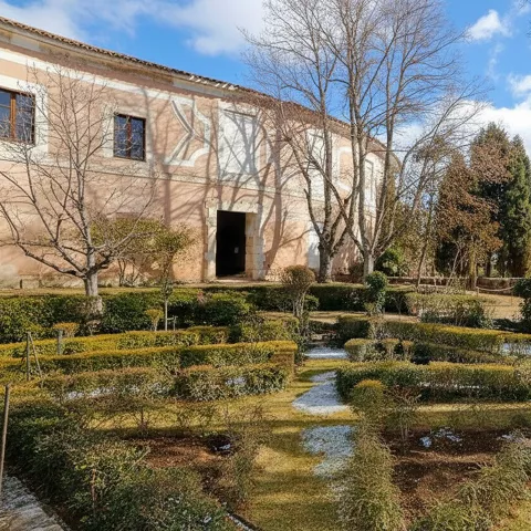 Jardines formales con setos bajos frente a edificio histórico de fachada clara.