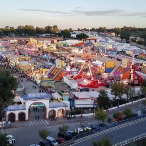 Vista aérea de feria con atracciones, luces y acceso principal.