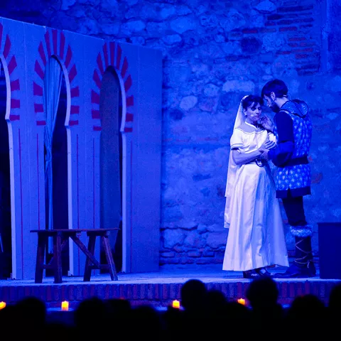 Escena teatral con pareja vestida de época bajo luz azul.