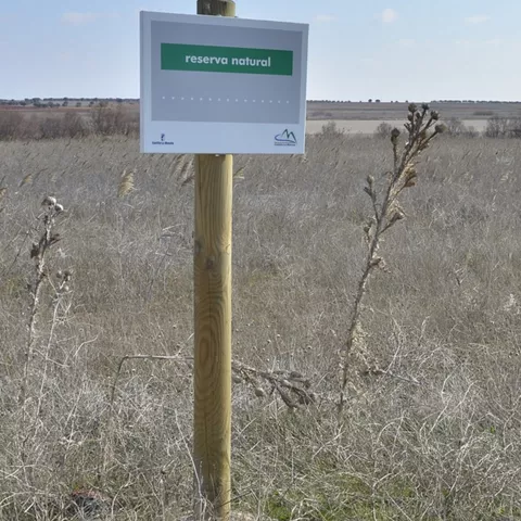 Cartel de reserva natural junto a una laguna y vegetación seca.