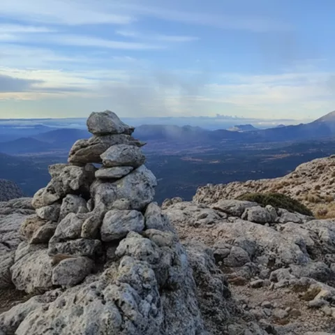 Montículo de piedras en primer plano con valle y montaña al fondo.