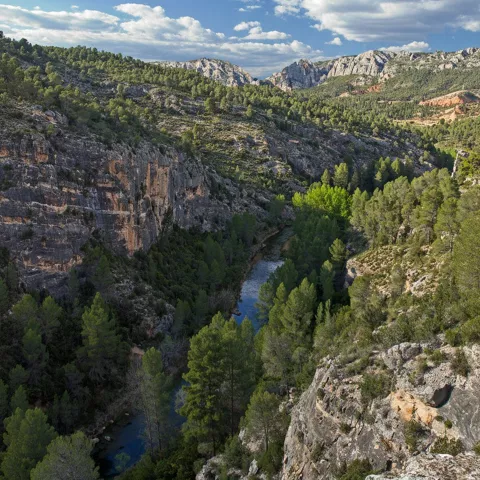 Valle profundo con río entre montañas y cielo azul.