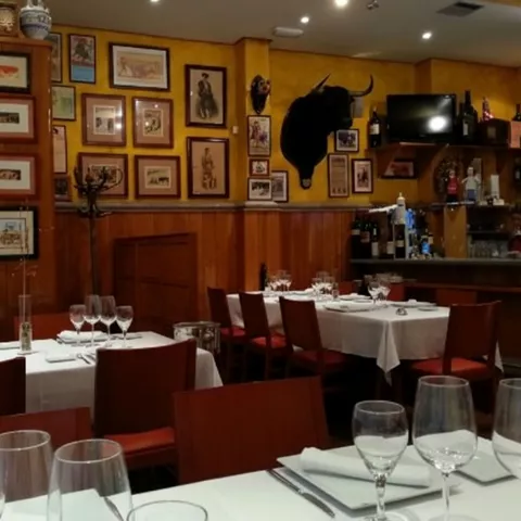 Salón de restaurante con mesas blancas y pared llena de cuadros.