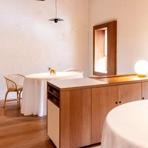 Sala de comedor con mesas vestidas, mobiliario de madera y techo visto.