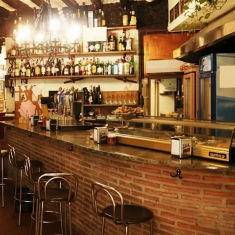 Barra de restaurante rústico con taburetes, botellas y embutidos colgados.