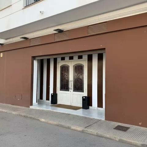 Entrada de local con puertas dobles y pared marrón, en una calle tranquila.