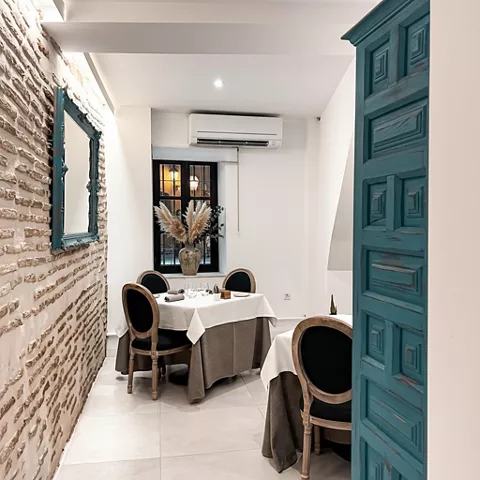 Pequeño comedor íntimo con mesa redonda, sillas tapizadas y puerta de madera azul.