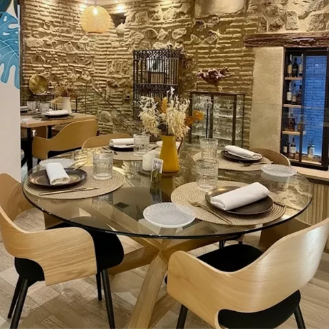 Mesa redonda vestida en salón con muros de piedra y luz cálida.